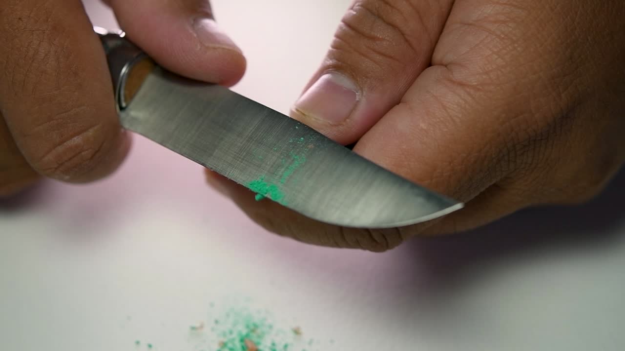 Footage of hands slowly sharpening a pencil and some coloured pencils with a sharp knife