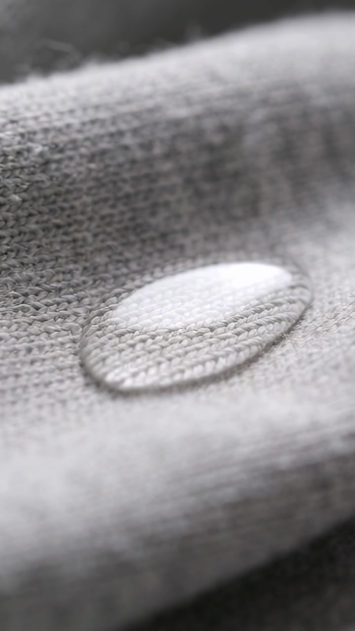 Vertical video: Droplet elongating with time passing on grey knit fabric, showing specular sheen