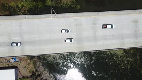 Drone-Rising-High-From-Bridge-while-Cars-Passing-High-Speed-Over-Clear-Water-Lagoon,-San-Mateo,-California