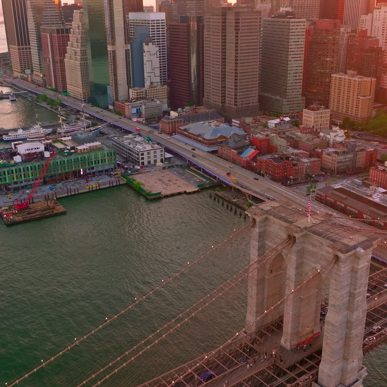 Manhattan Island in the rays of setting sun. Drone flying over the majestic Brooklyn Bridge and docks