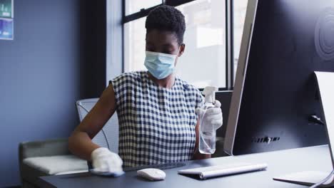 Mujer-Afroamericana-Con-Mascarilla-Y-Guantes-Desinfectando-Su-Estación-De-Trabajo