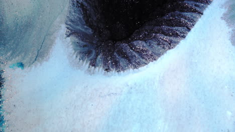 a dark, swirling crater surrounded by icy blue textures and glittering highlights evokes mystery