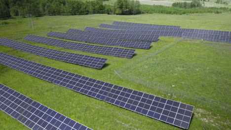 Descending-aerial-of-large-solar-power-plant-farm-on-green-grass-field-in-wilderness-during-sunny-day