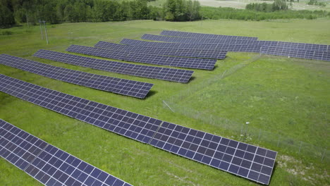 descending aerial of large solar power plant farm on green grass field in wilderness during sunny day