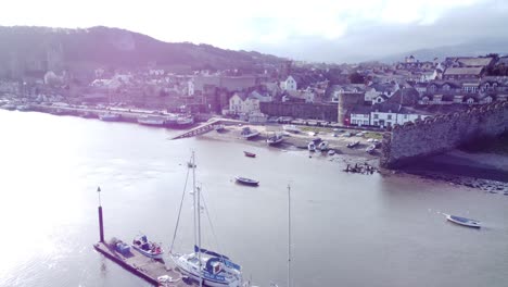 idyllic conwy castle and harbour fishing town boats on coastal waterfront aerial fly over boats below