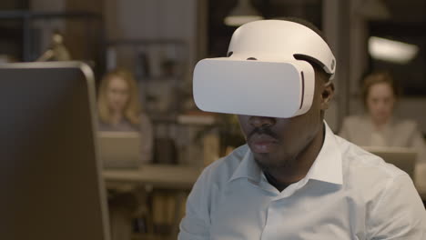vista ravvicinata dell'uomo americano seduto alla scrivania in ufficio con occhiali per realtà virtuale 2