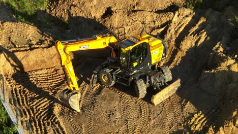 aerial drone view of jcb excavator on a construction site, digging and moving earth with visible track marks in the soil, highlighting heavy machinery in action. (4k)