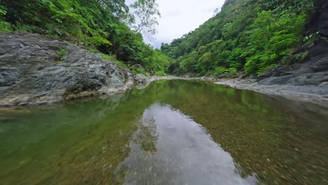 Low-drone-flight-over-reflective-river-in-tropical-green-rainforest,-dolly-in