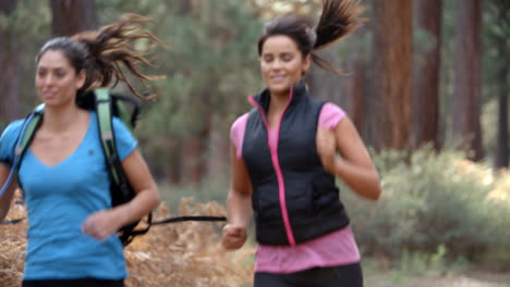 dos mujeres jóvenes corriendo en un bosque, de cerca