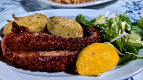 hearty meat platter with braised octopus and salad served with potato and greens on rustic wooden table at sunset outdoors