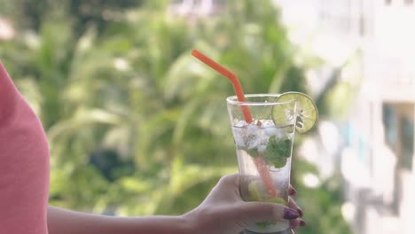 young lady in pink blouse bends over and sips cool mojito