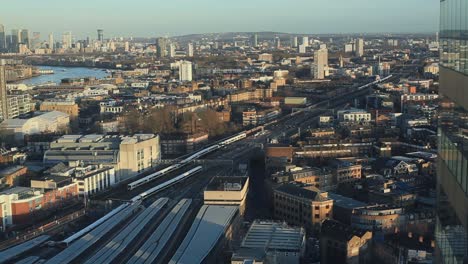 speed ramped video of a train station. white trains look like snakes. amid busy city, river floats peacefully. sun is setting, spilling orange light on london. filmed above london bridge, uk