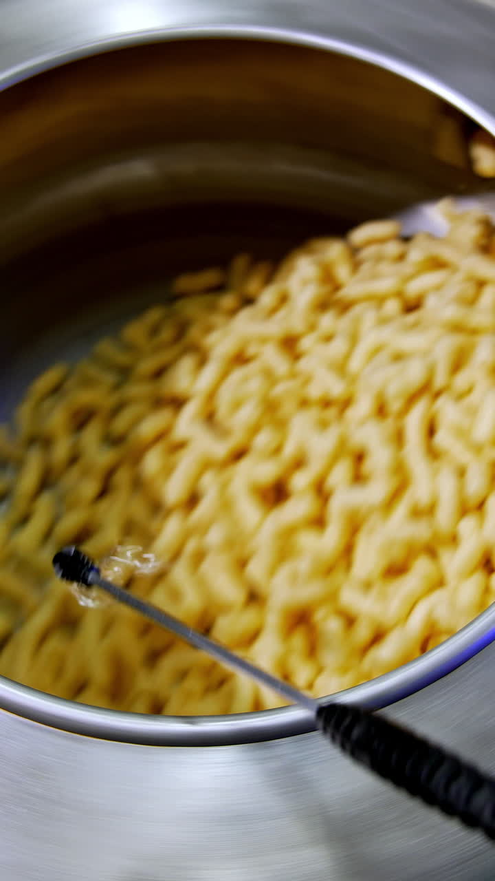 Spinning metal tank filled with yellow crispy snacks. Pulverize device spraying sugar glazing on corn sticks. Food factory manufacturing. Vertical video