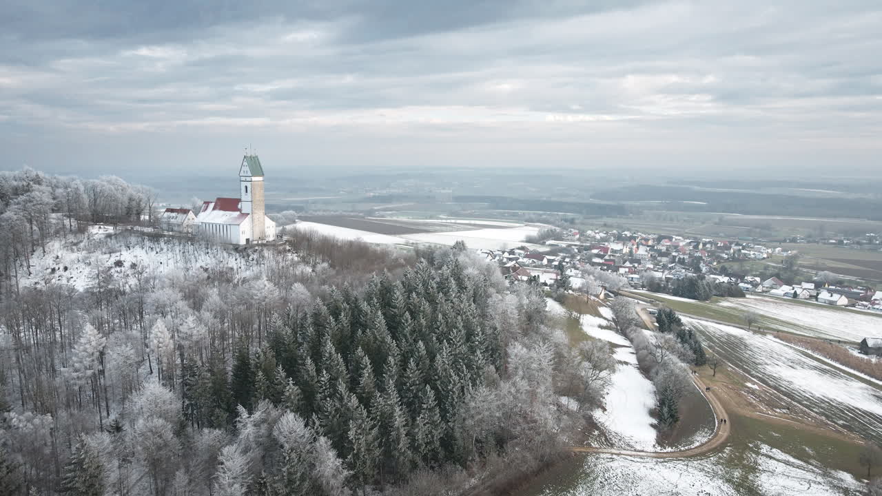 Drone skifter til højre og afslører den markante hvide tårnkirke med rødt tag oven på den frostklædte bakke i Utterweiler, Baden-Württemberg, omkranset af tætte rimfrosttræer med udsigt over sneklædt mark