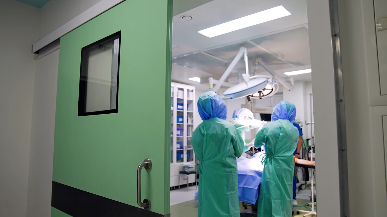 Equipo quirúrgico trabajando en el quirófano, vendando la pierna del paciente. Grabación desde la puerta abierta de la sala de cirugía