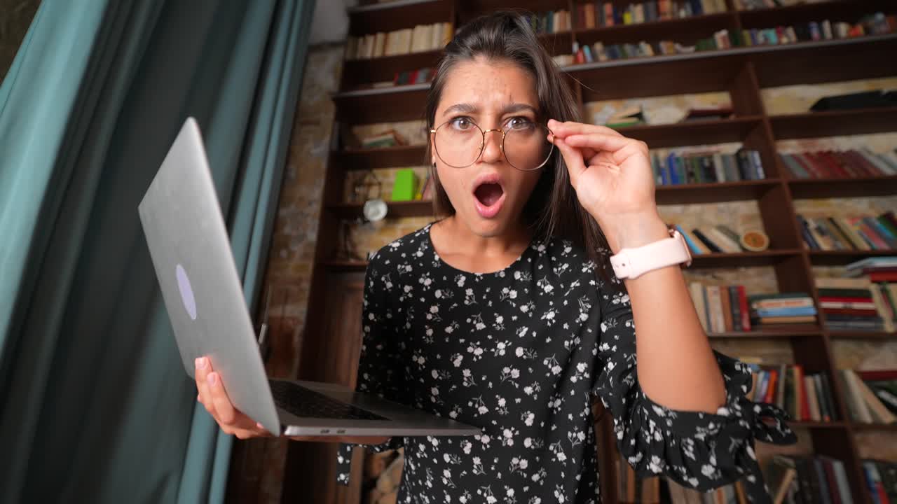 mujer mirando con conmoción a la computadora portátil en una biblioteca
