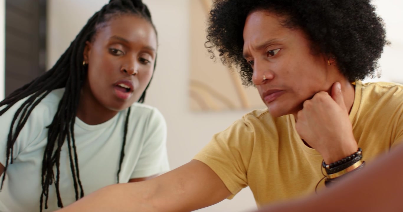 African couple at dining table, woman showing blue phone while man pointing, deciding pizza board