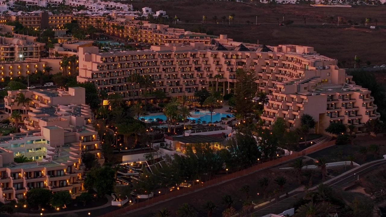 Una vista aerea cattura il vasto complesso turistico di Costa Teguise a Lanzarote durante le tranquille ore del crepuscolo. I numerosi edifici alberghieri, illuminati da luci calde, presentano molti