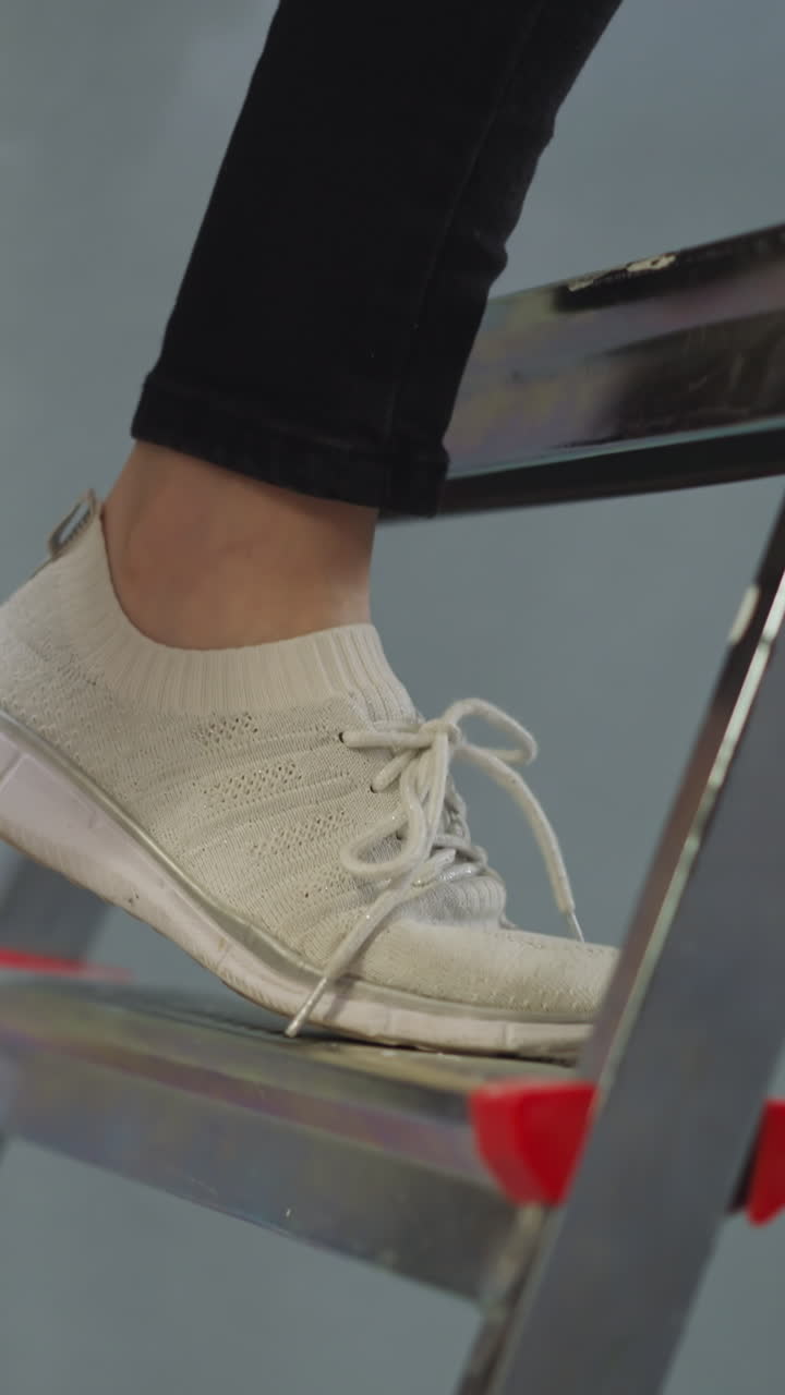 Woman with bucket of paint climbs up step ladder in room closeup. Handy-woman does repair in apartment. Supplies and tools for handmade renovation