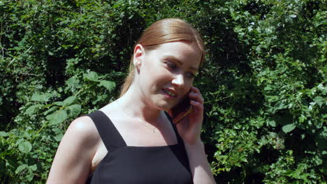 An-excited-red-haired-girl-talking-on-a-phone-outside-in-nature