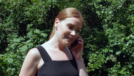 an excited red haired girl talking on a phone outside in nature