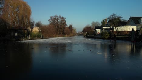 drone flying under the wooden bridge towards the people skating in the frozen river