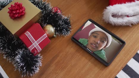 Smiling-african-american-boy-wearing-santa-hat-on-christmas-video-call-on-tablet