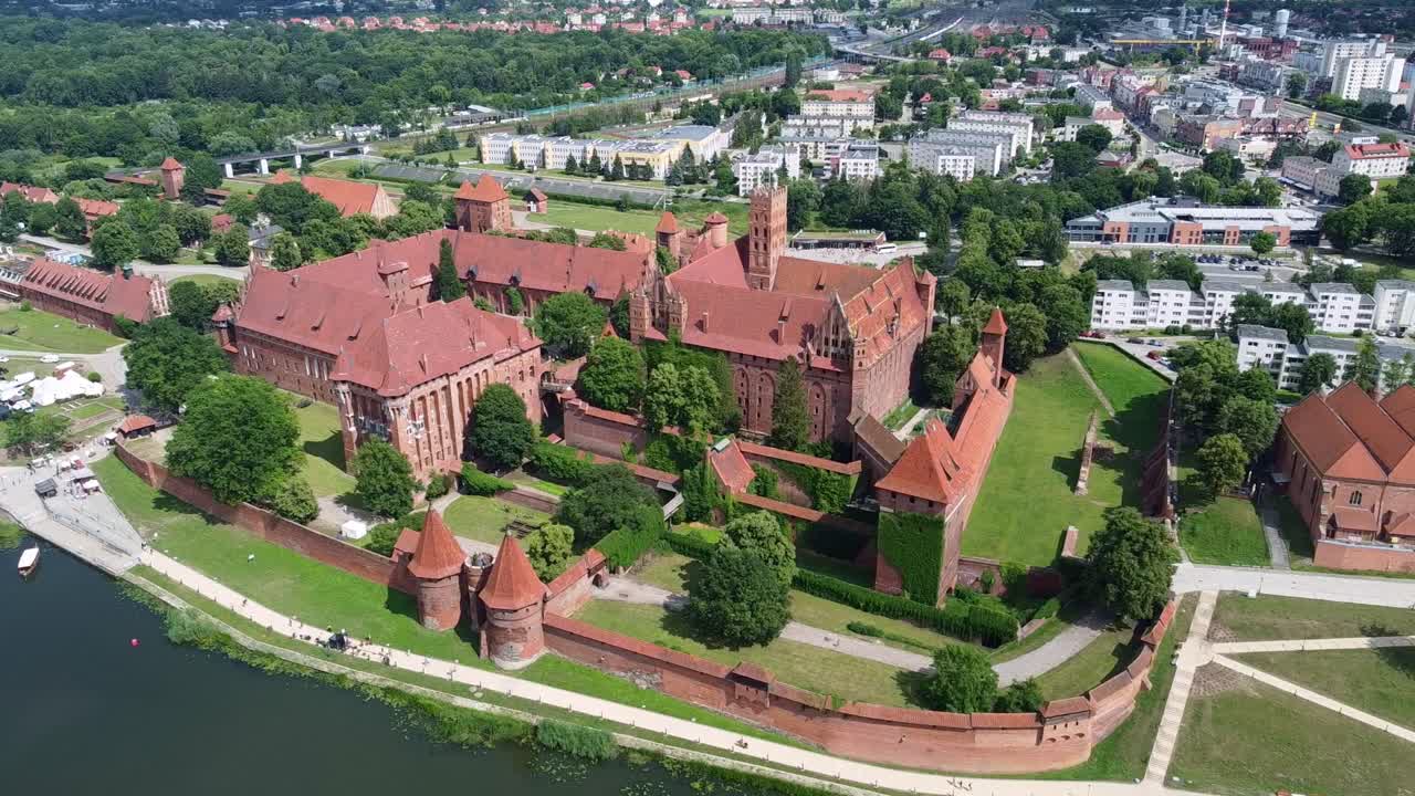Aerial of Malbork Castle, world largest castle by area, a UNESCO World Heritage Site in Poland along river on sunny day, establishing orbit
