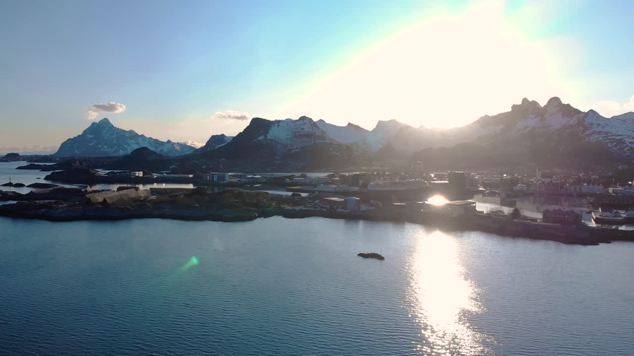 Aerial drone shot of the blue ocean in Lofoten, Norway with rocks in the foreground and mountains in the background. And sunset in the sky