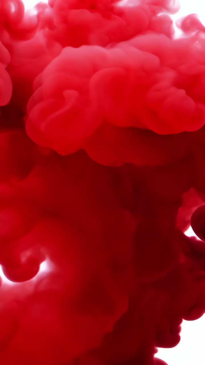 Red Smoke Cloud Formation on White Background. Bright red smoke billows upward against a white backdrop, creating a striking visual effect. Vertical video