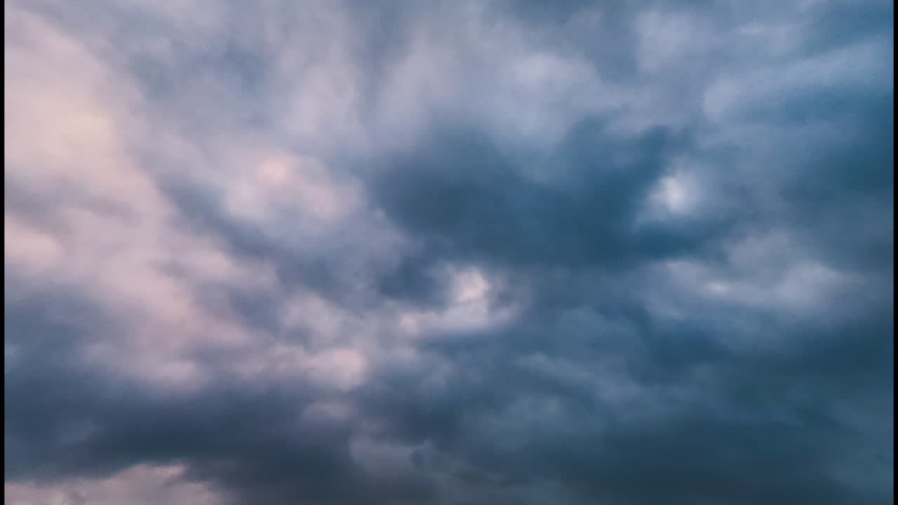 Grey, orange and pink cloudscape in the sky. Thick dark clouds float in the horizon. Low angle view. Timelapse.