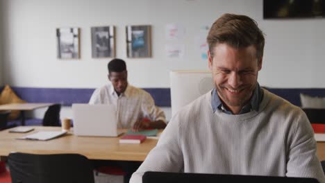happy caucasian businessman sitting at table and using laptop at office