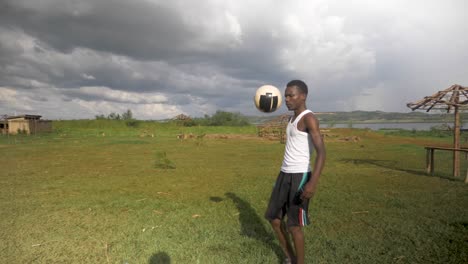 slow motion wide shot of a young african man doing kick ups on a beach by a lake with storm clouds rolling in