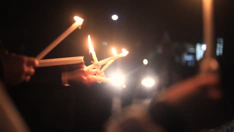 close up of group of people's hands holding lit white candles together on dark evening