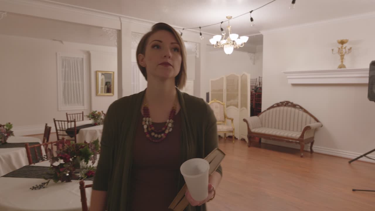 A woman is seen moving around tables and chairs. She looks around to see if anyone is there