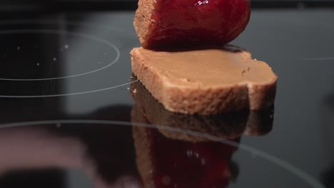 a peanut butter and strawberry jam sandwich being squished together on a black surface