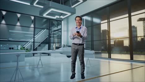 full body of an asian male professional worker standing with his smartphone with drone project, high-tech industrial facility, he is looking at the camera with a smile