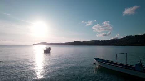 Drone-Aéreo-Pasando-2-Barcos-Hacia-La-Puesta-De-Sol-A-Una-Isla