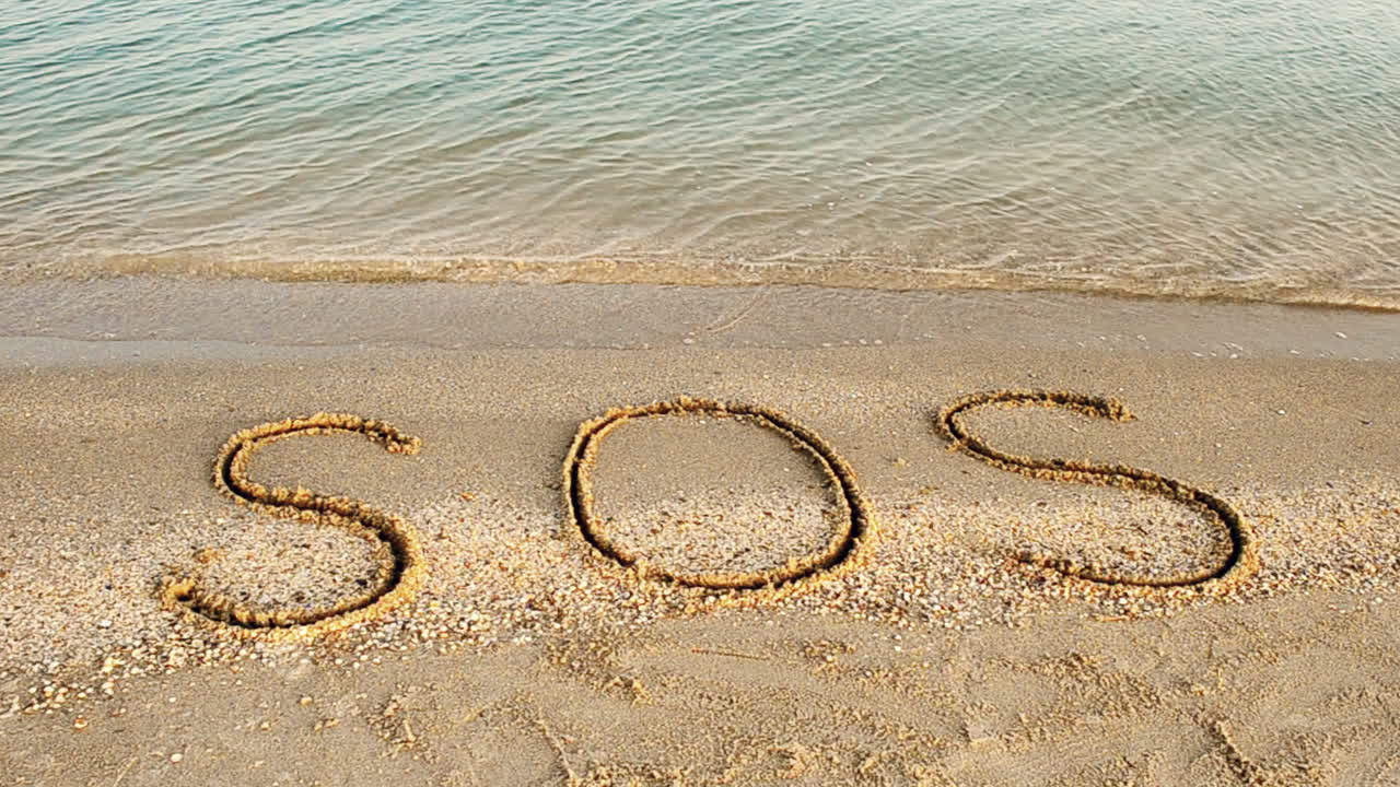 Inskriptionen SOS i sanden. Filmning på stranden