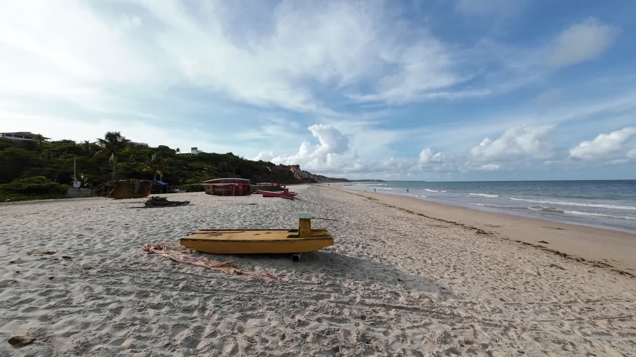 Handheld action camera shot of the tropical popular destination Love Beach with golden sand, cliffs, turquoise water, and small fishing boats in the beautiful Conde, Paraiba, Brazil on a summer day