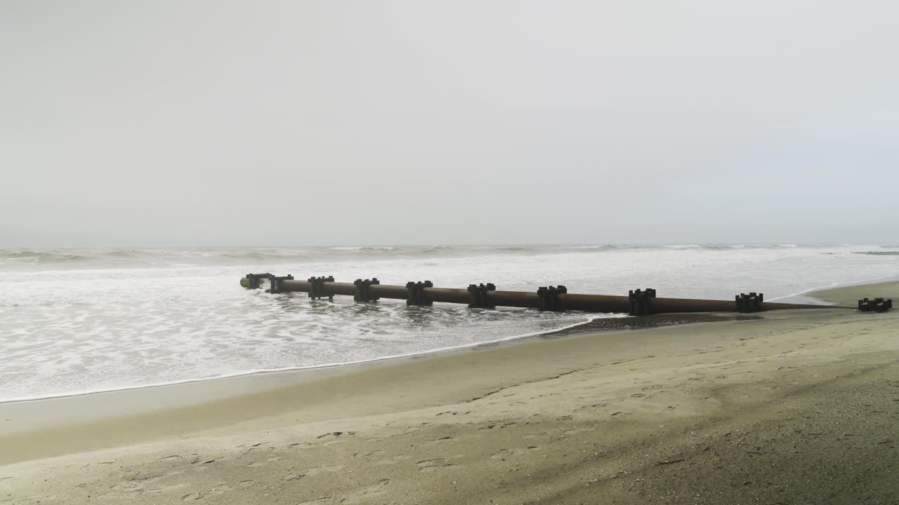 Ocean waves hitting pipeline on beach on a gloomy day in OCNJ