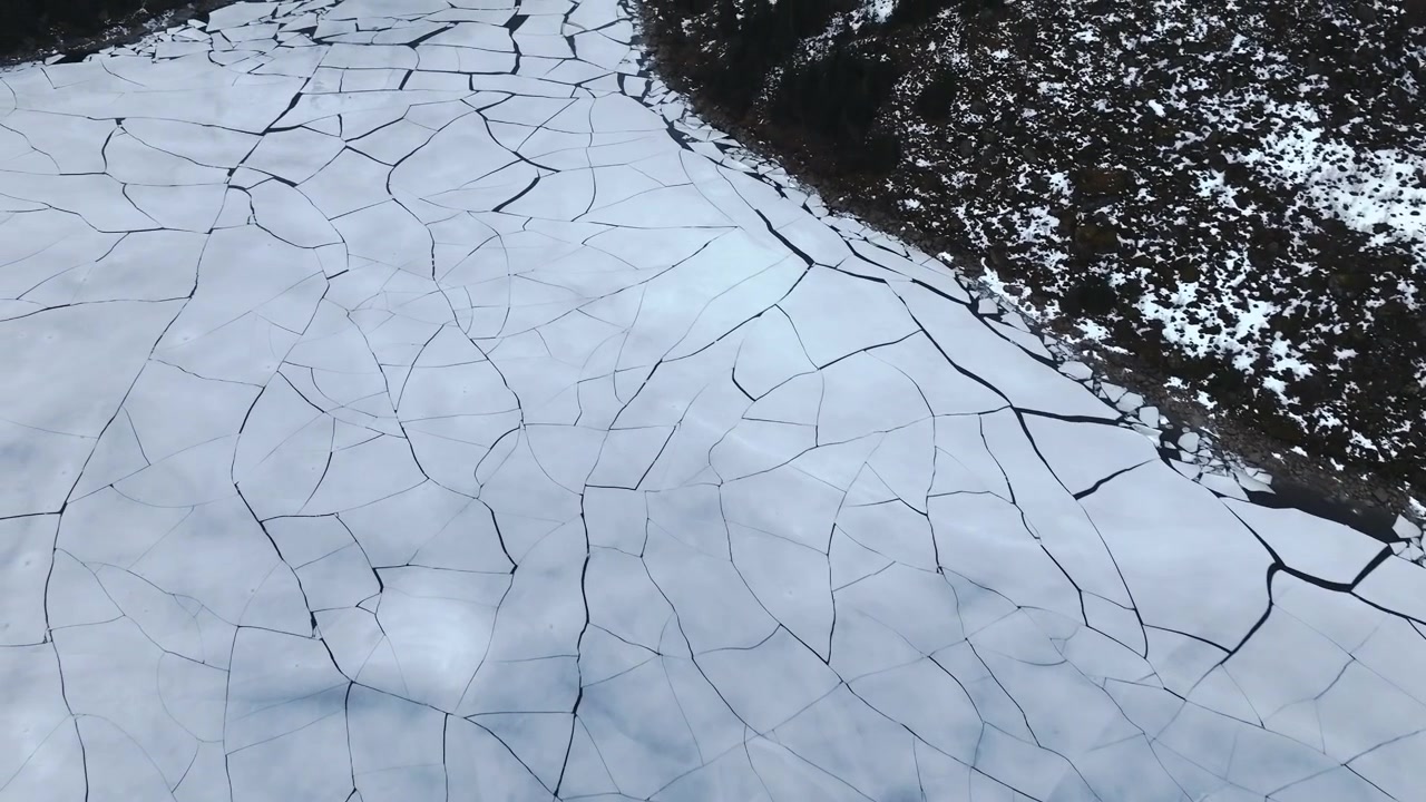 Stortvatnet lake on Austvagoya in Vagan Nordland Norway displays fractured ice sheet with thermal contraction cracks and reflective surface near shore, top down macro aerial shot