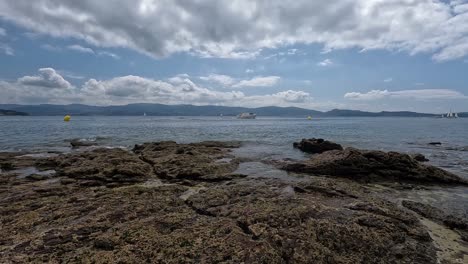 Eine-Teure-Yacht-Segelt-Zwischen-Den-Gelben-Blasen-Auf-Die-Segelboote-Zu,-Das-Meer-Ist-Ruhig,-Im-Hintergrund-Sieht-Man-Die-Berge,-Tag-Mit-Schwammigen-Wolken,-Kamerafahrt