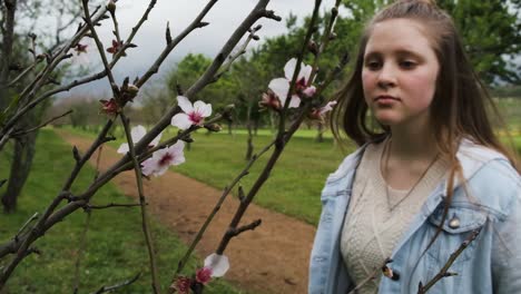 Slow-motion-casual-young-girl-smelling-fresh-scented-pink-flower-blossoms-on-tree