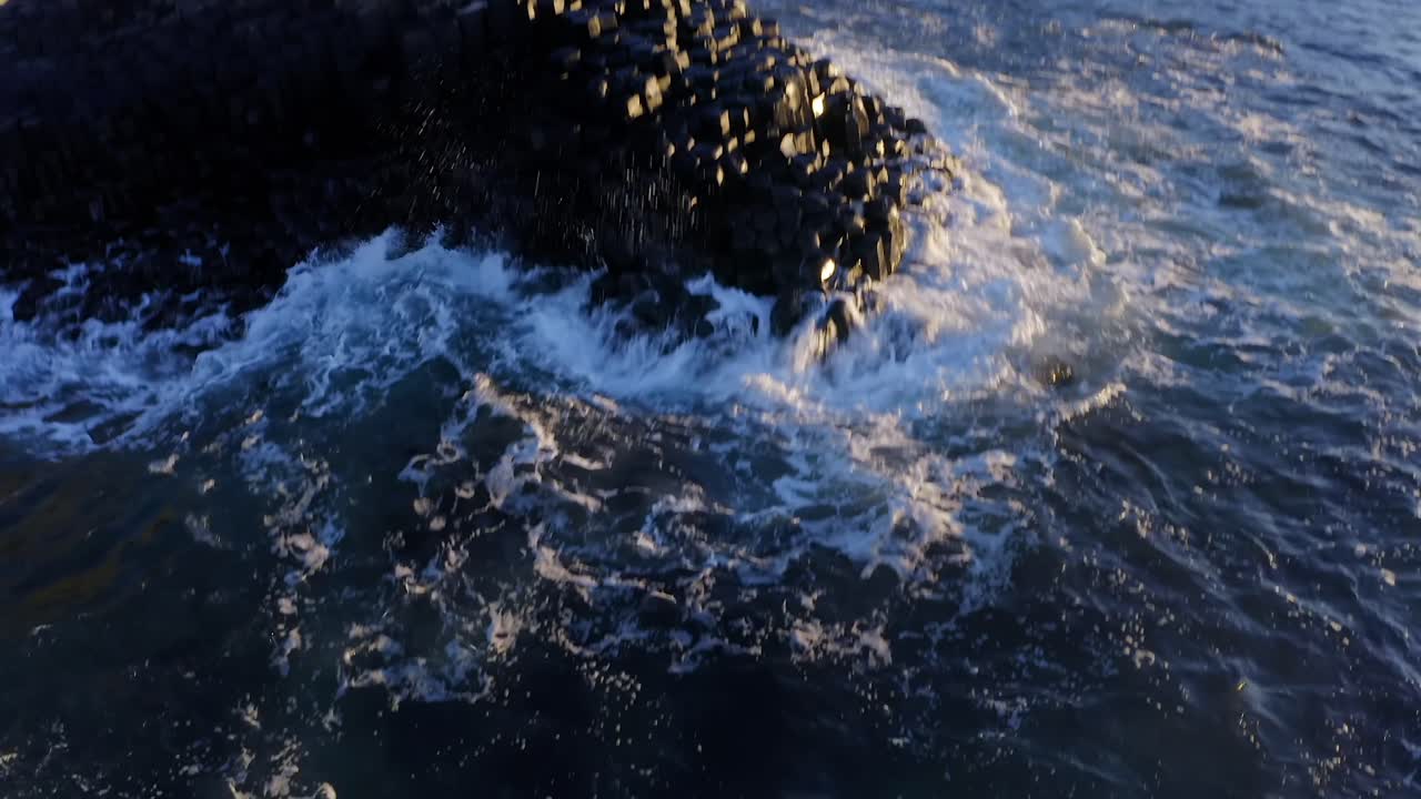 Aerial glide over the basalt rock formations along the shoreline of Giant's Causeway, showcasing the rugged beauty of the coast.