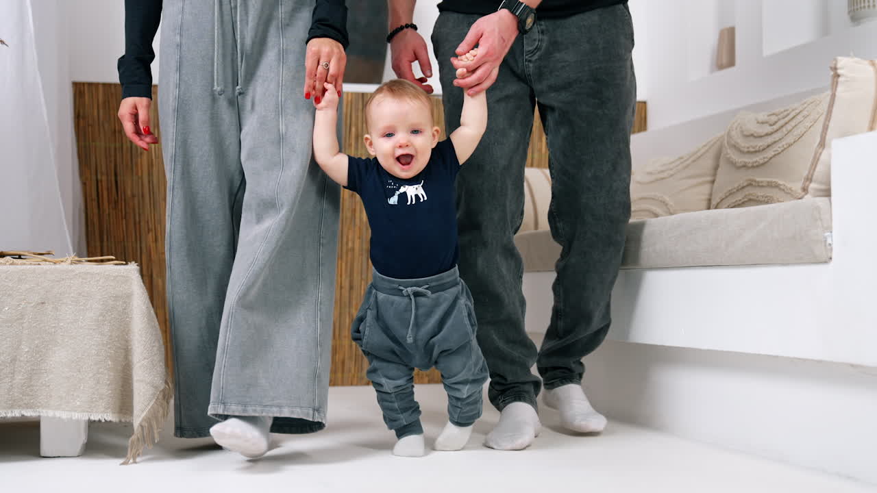Adorable smiling baby is happy to step supported by his parents. Cute infant starting to walk.
