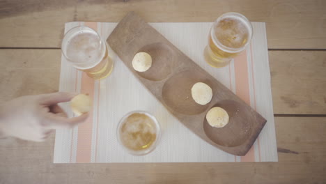 personas horneando pan chipa juntos en una mesa de madera, disfrutando de cerveza y bocadillos caseros, capturando la alegría de la unión sobre la comida