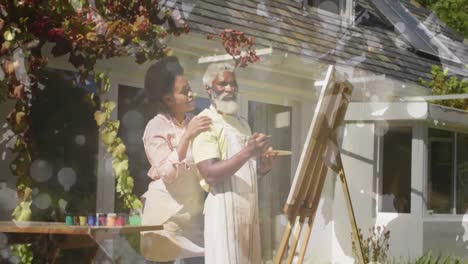 Animation-of-light-spots-over-african-american-couple-painting-on-easel-in-garden