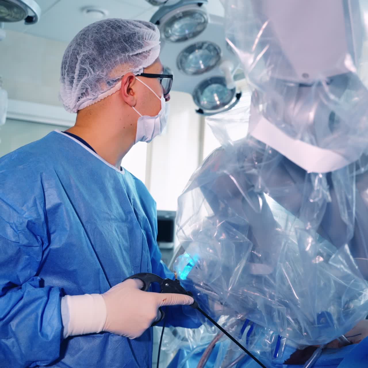 Medical specialist near the robotic device. Surgeon in blue protective uniform controls the work of medical robot on the screen.