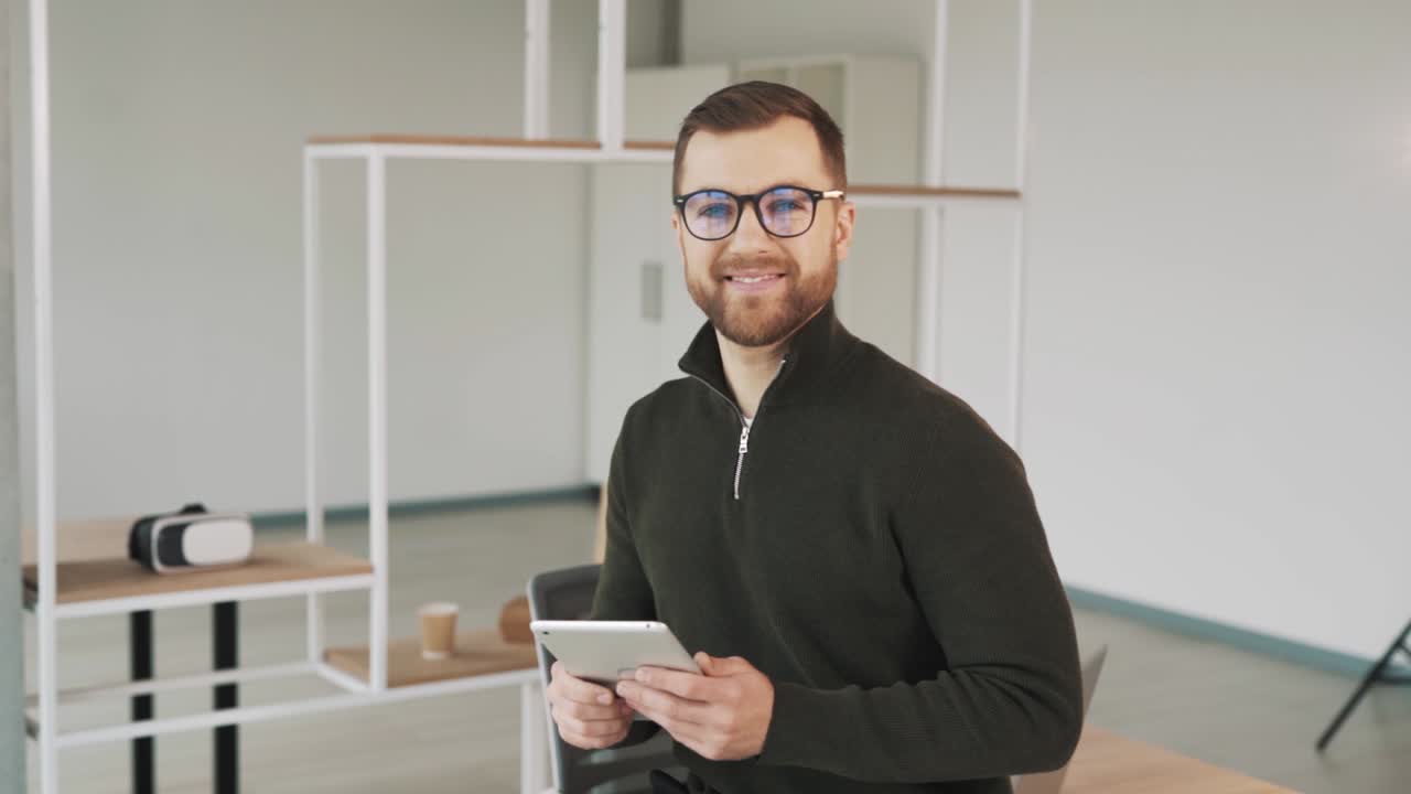 A charming, cheerful, and charismatic man with a tablet is looking into the camera and smiling